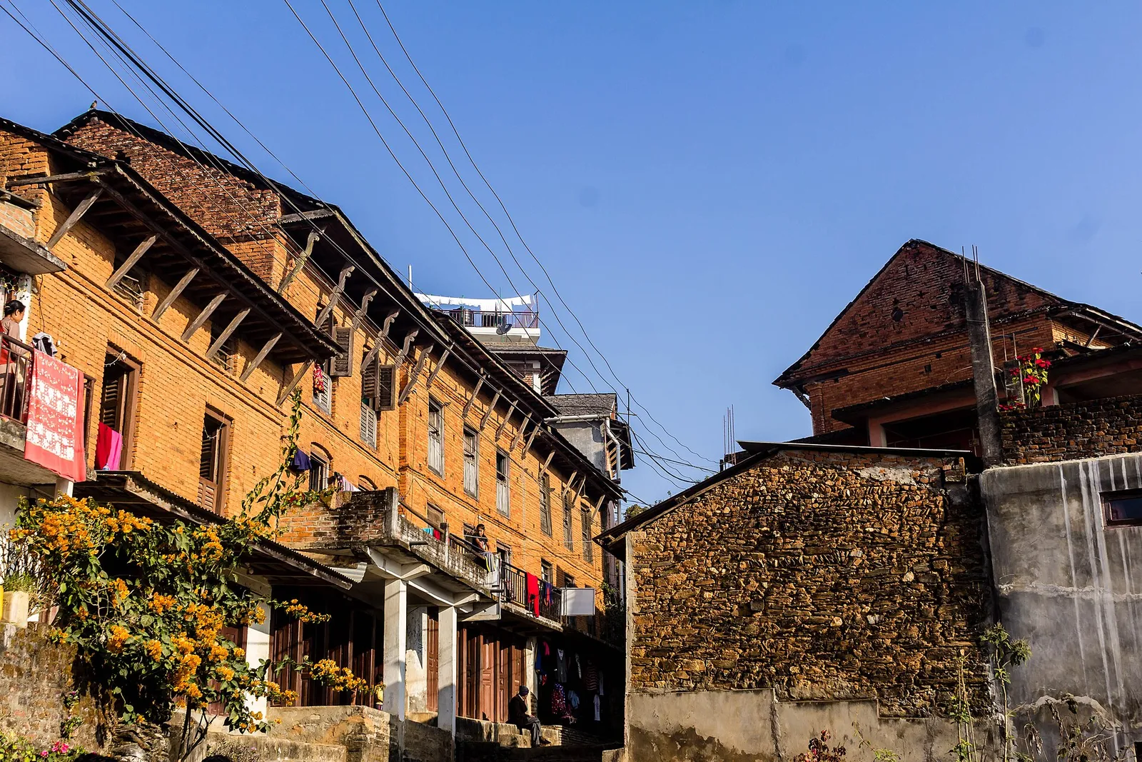 Old brick Newar houses with wooden balconies and flowering shrubs along a lane in Bandipur