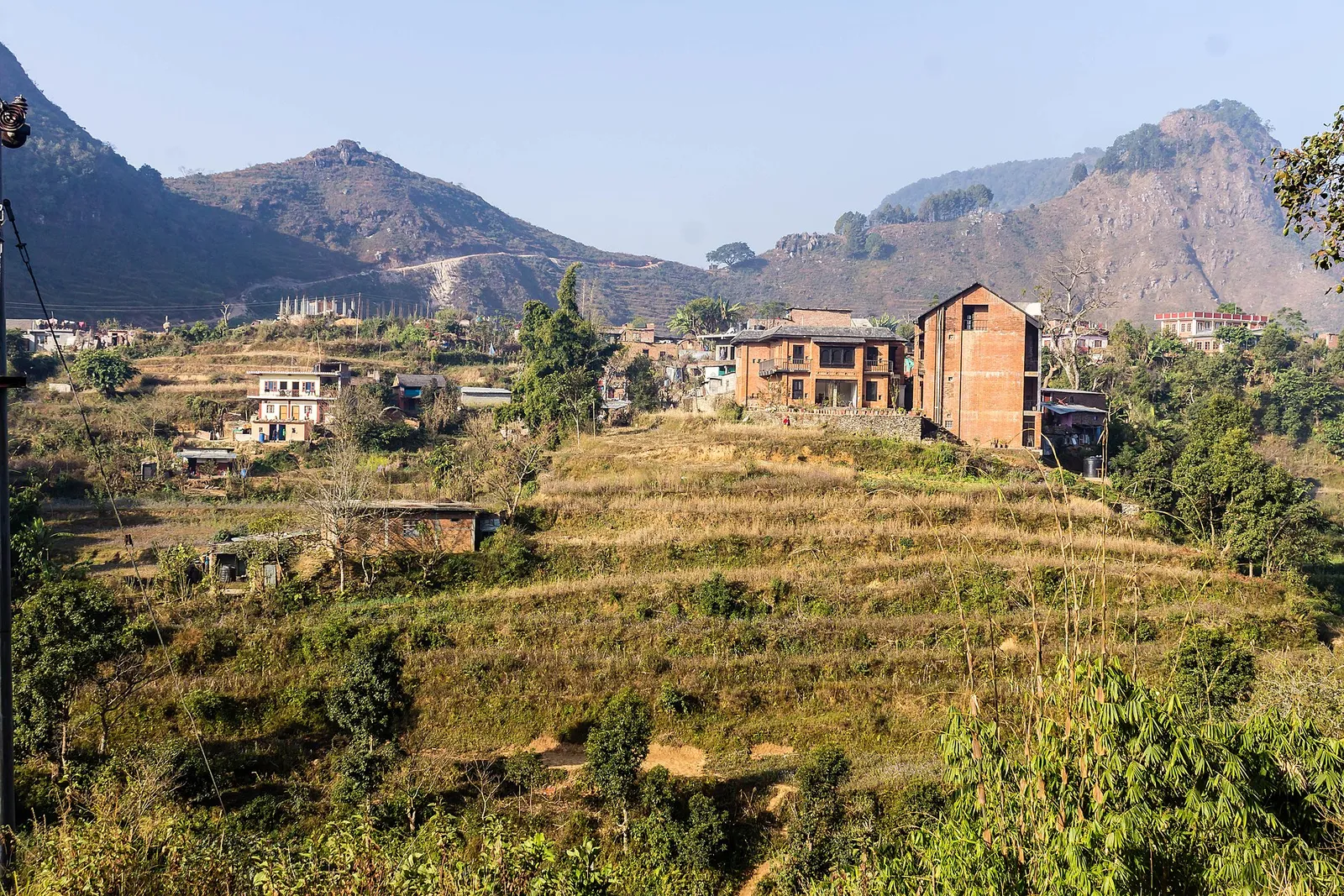 Terraced fields climbing a hillside to brick houses, with rocky ridges behind, near Bandipur