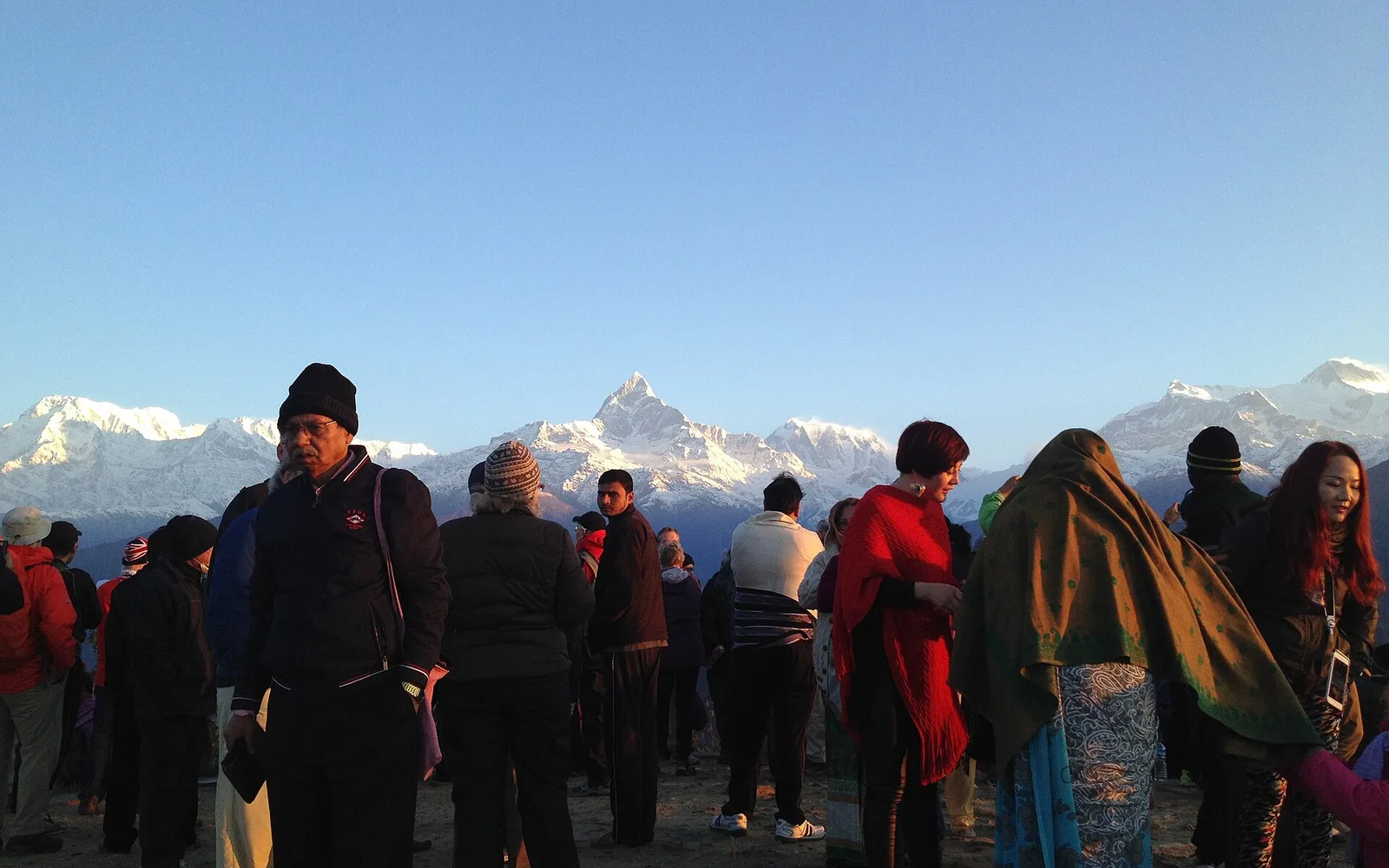 A crowd at a hilltop viewpoint at dawn with Machhapuchhre and the Annapurna range behind them