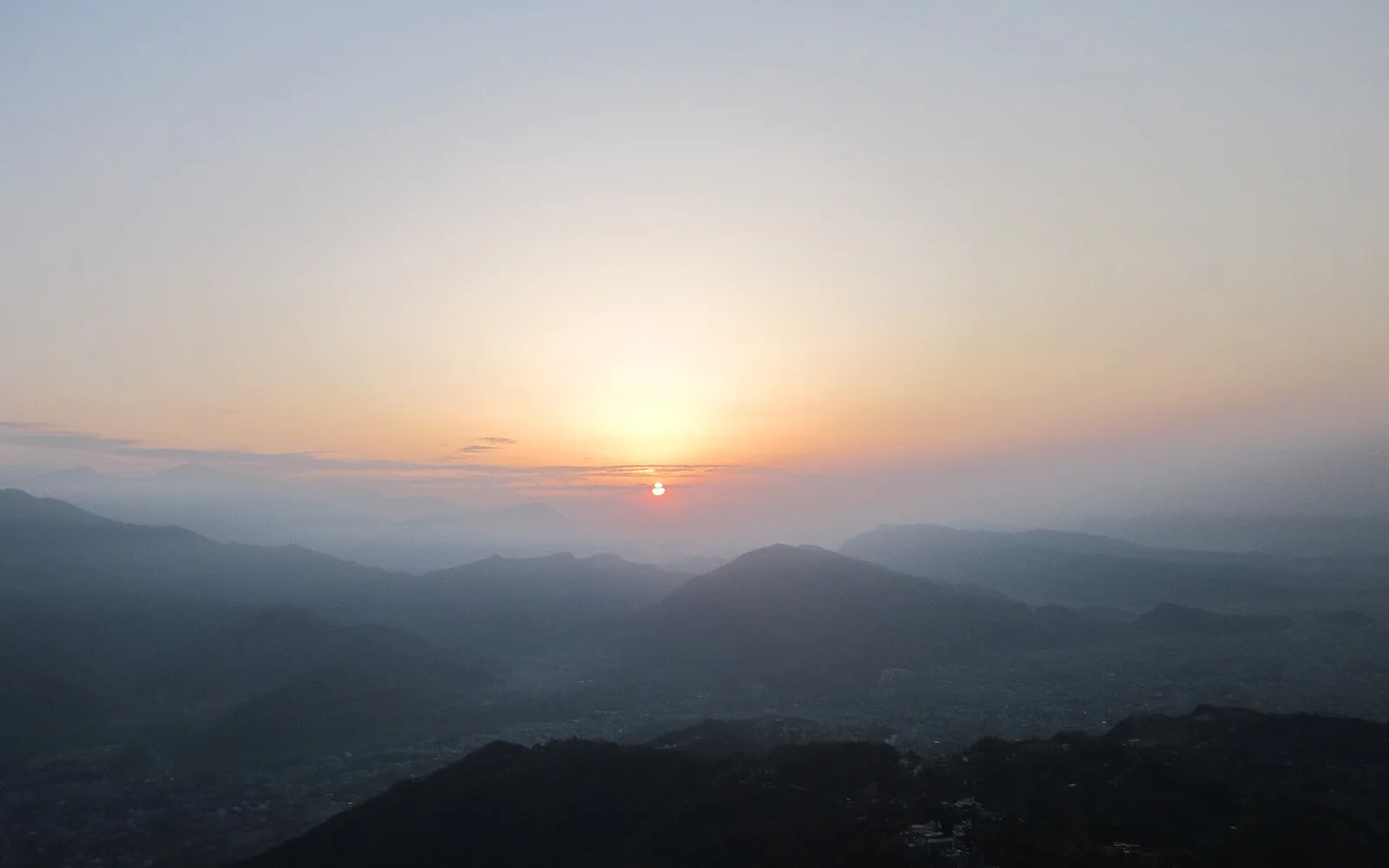 The sun rising over layered hazy hills seen from Sarangkot