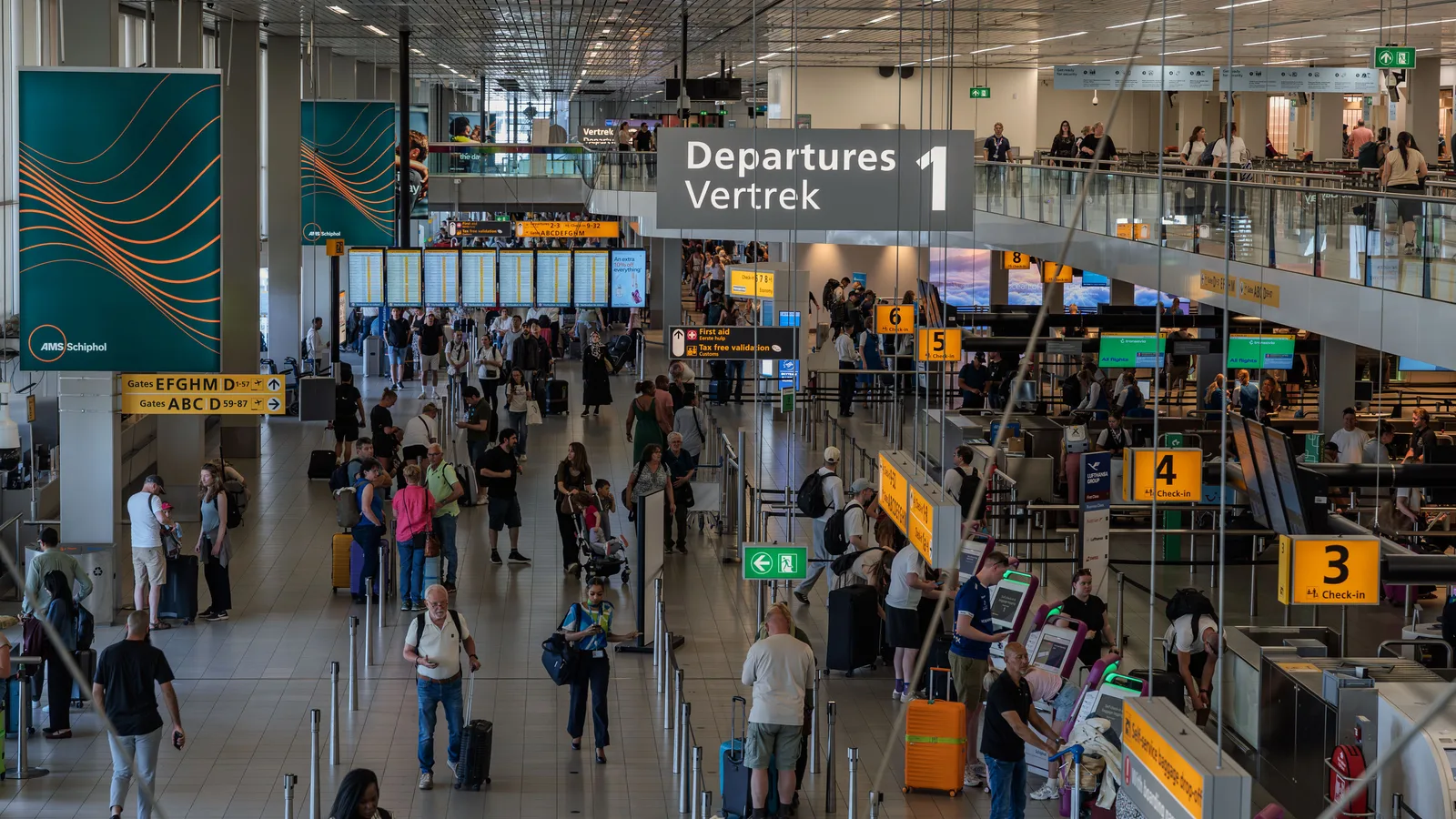 Departures hall at Amsterdam Schiphol with check-in queues under the flight information boards
