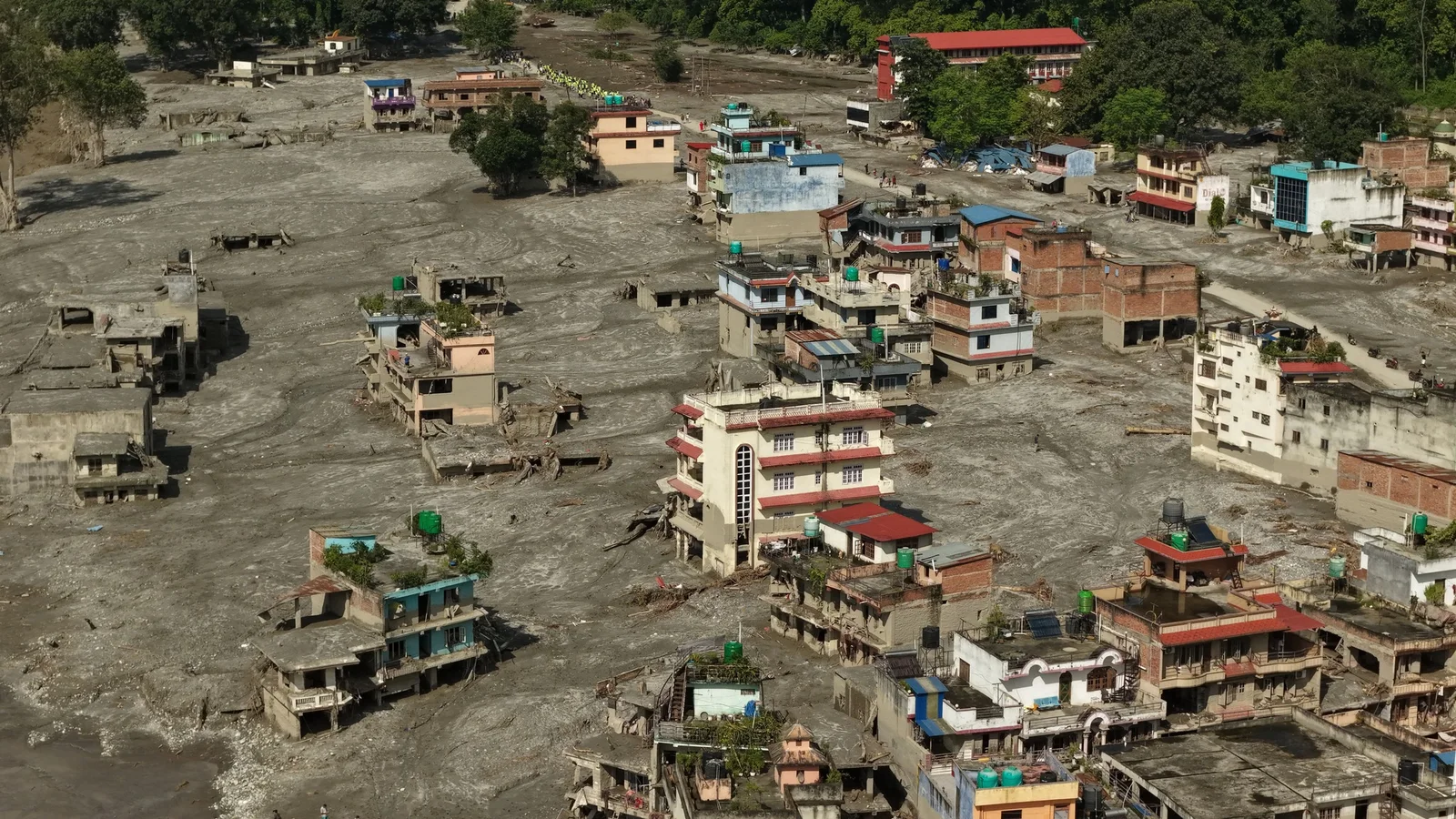 Drone view of Devighat in Nuwakot district after the 26 August 2026 Bhote Koshi flood, with multi-storey buildings standing intact while the ground around them is buried metres deep in grey silt. Photograph shared on Instagram.