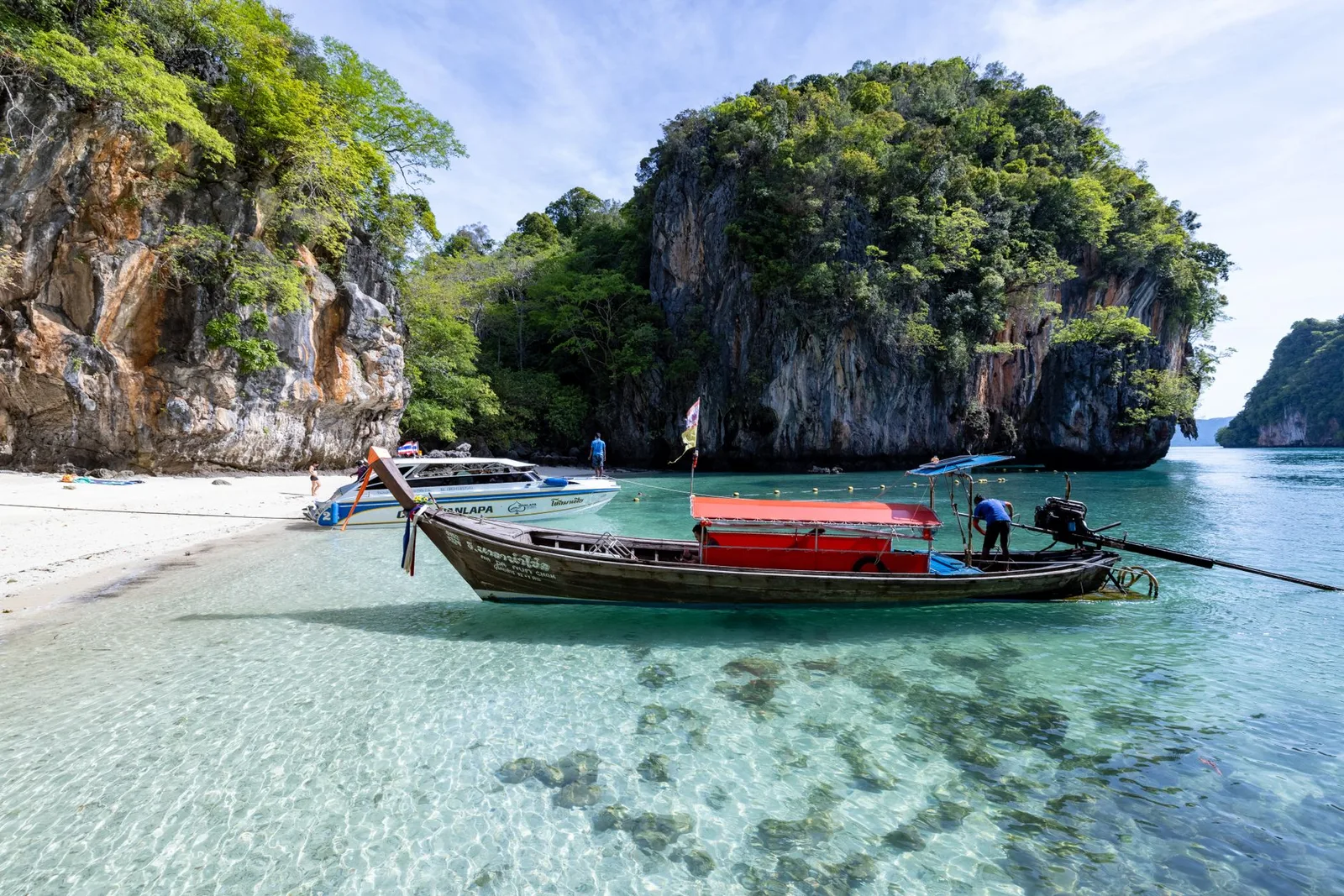 A turquoise tropical bay with limestone karst islands and a wooden longtail boat in southern Thailand — an iconic Southeast Asia coast scene