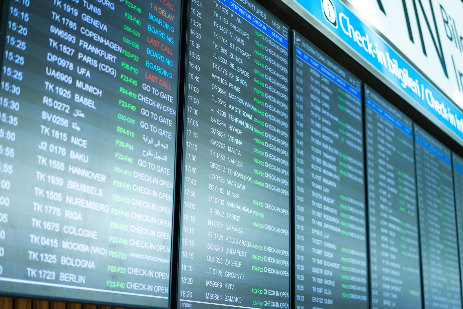 An airport departures board above a busy terminal — timing when to book flights, 2026