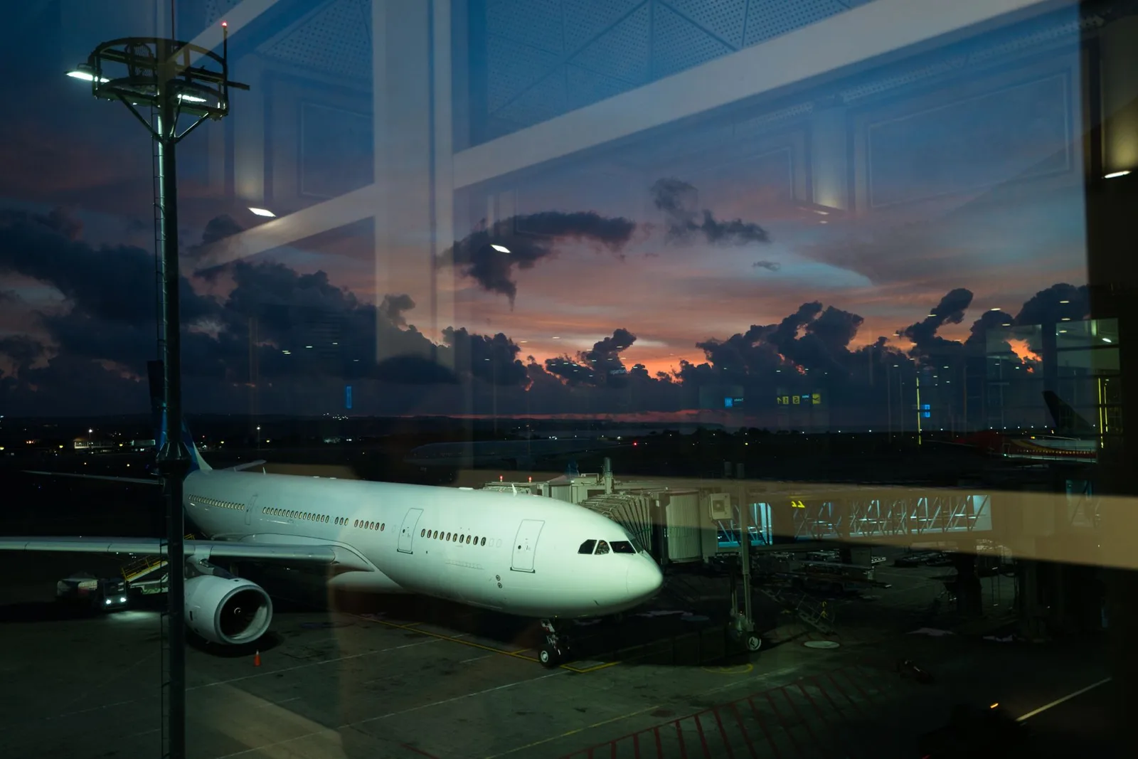 A passenger aircraft parked at an airport hub gate at dusk with a city visible beyond — the connecting airport where a long layover can become a free multi-day stopover