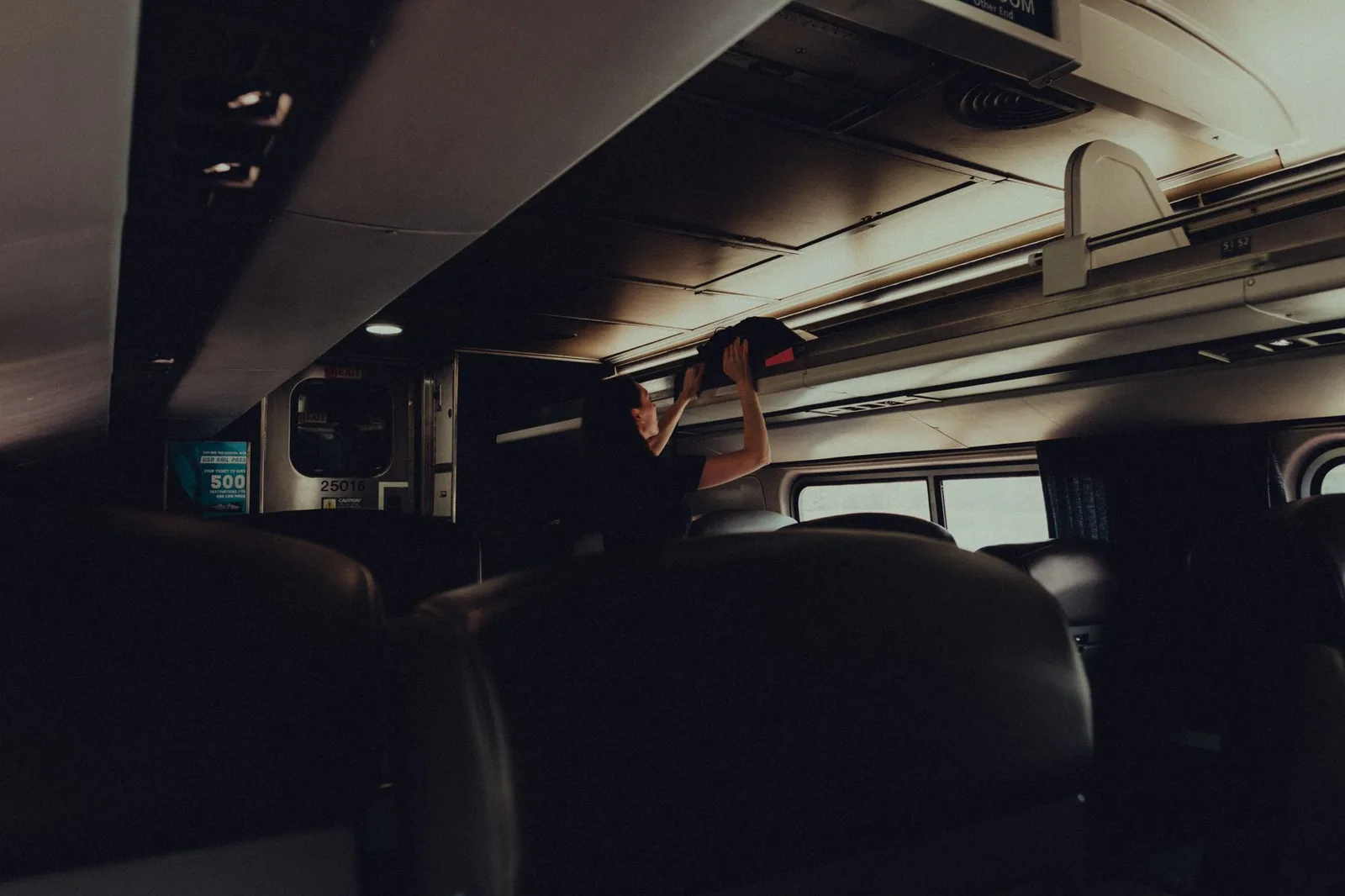 A traveller lifting a wheeled cabin bag into an aircraft overhead locker