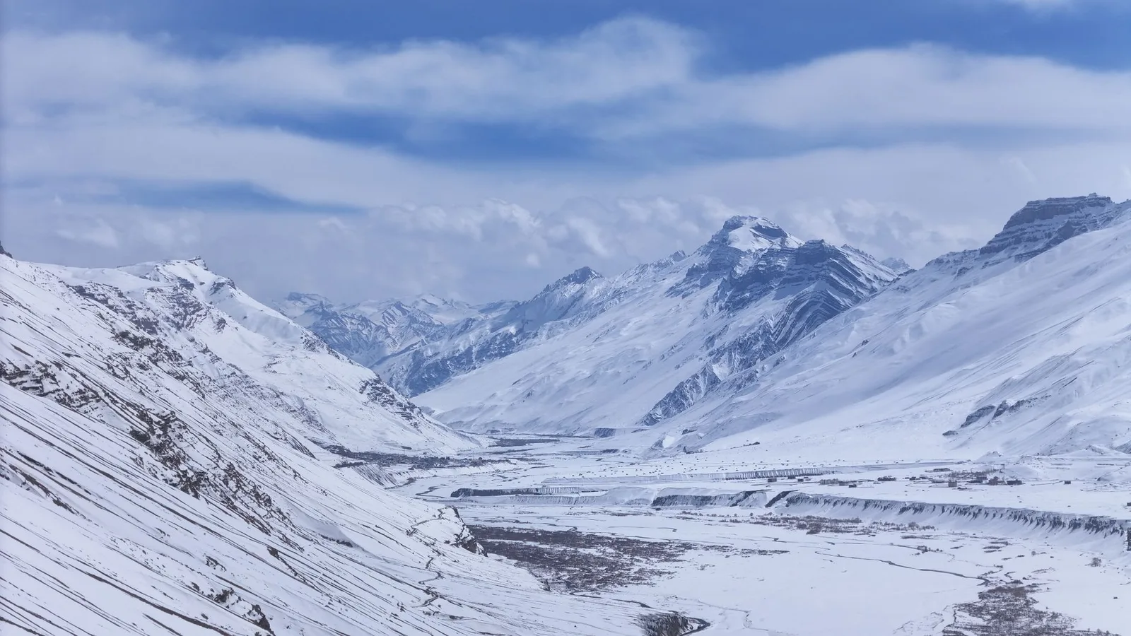 A sweeping view of the snow-capped Nepal Himalaya with a debris-strewn glacier winding down a high mountain valley