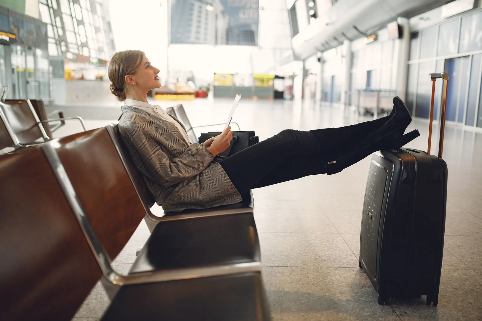 A traveller checking a flight on a smartphone beside an airport departures board — for popular routes, last-minute fares usually rise rather than fall
