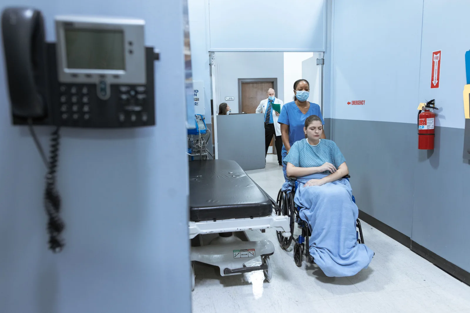A nurse assists a patient in a wheelchair along a hospital corridor — medical tourism cost comparison, 2026