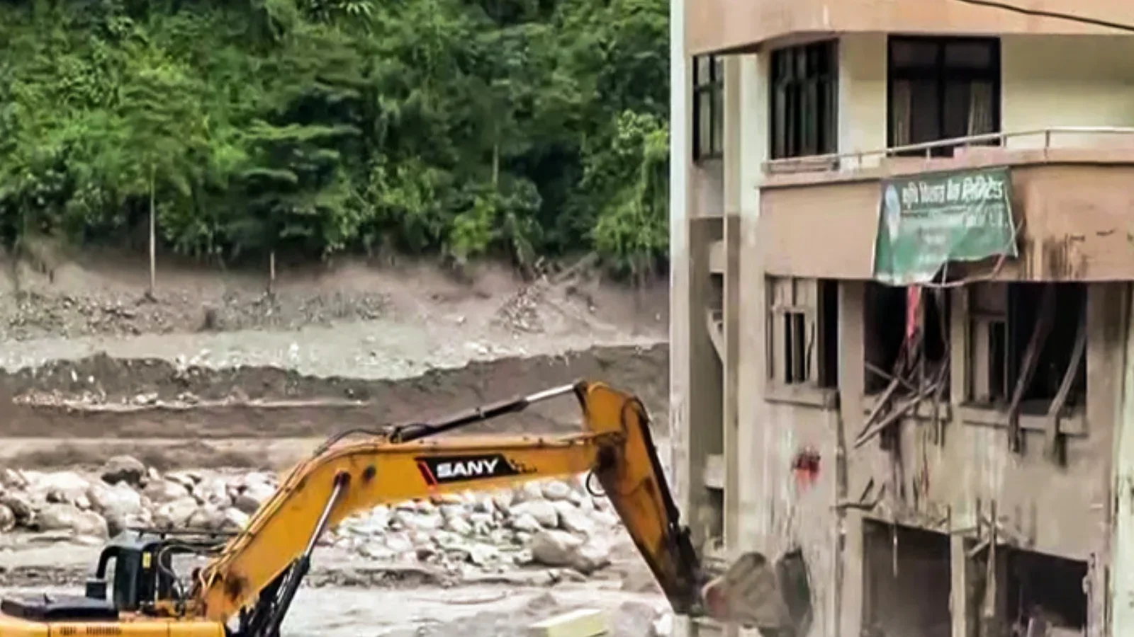 An excavator digs silt and boulders from beside a gutted concrete bank building in the Bhote Koshi flood zone, its lower floors torn open. Photograph shared on Instagram