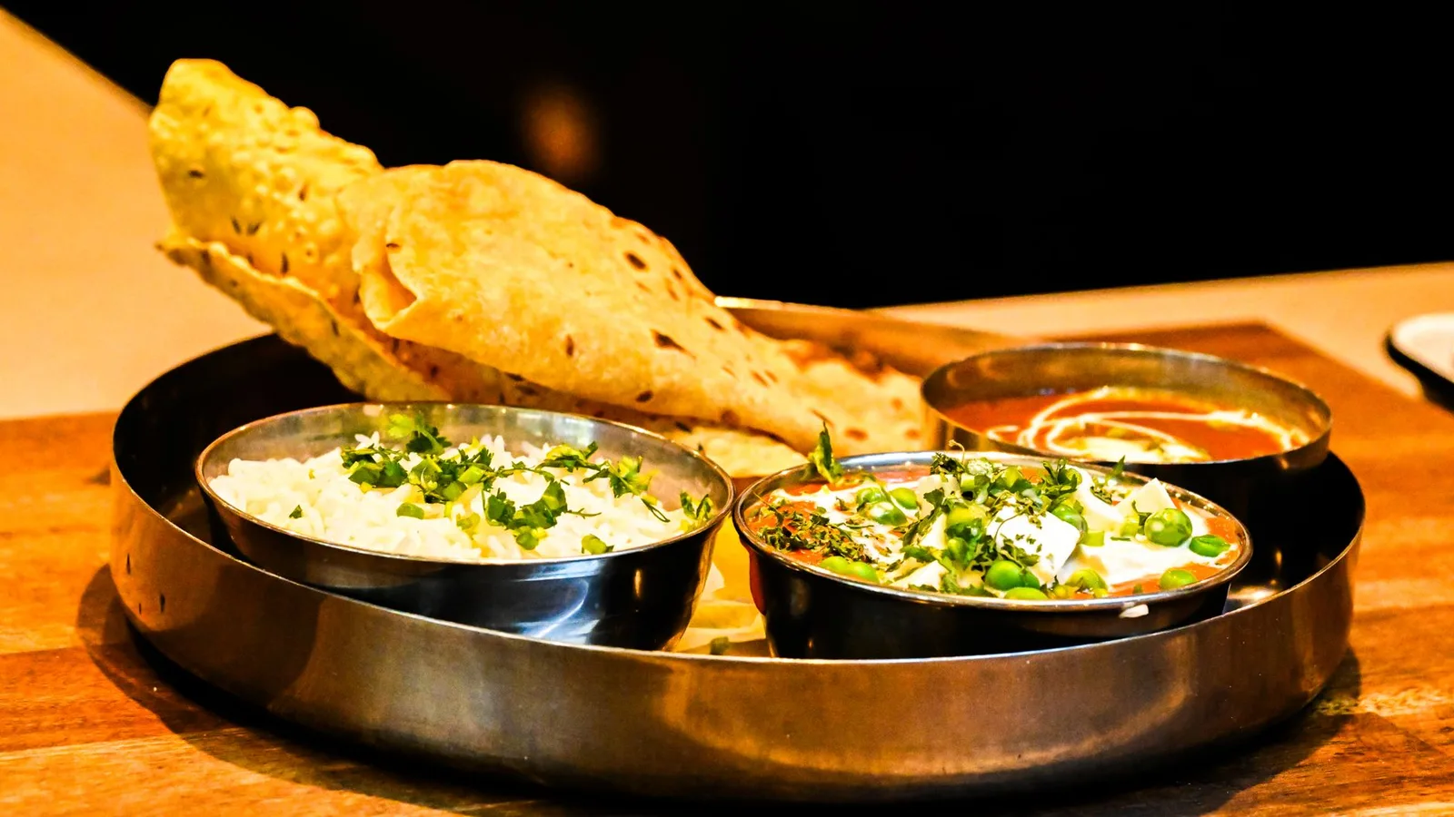 A steel thali plate of rice, lentil and vegetable curries and a crisp papad - a Nepali dal bhat meal