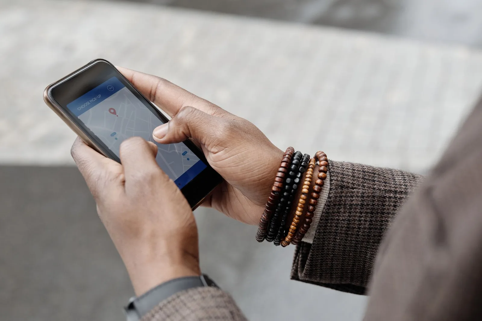 A traveller holding a smartphone showing a navigation map on a trail, with a folded paper map in hand