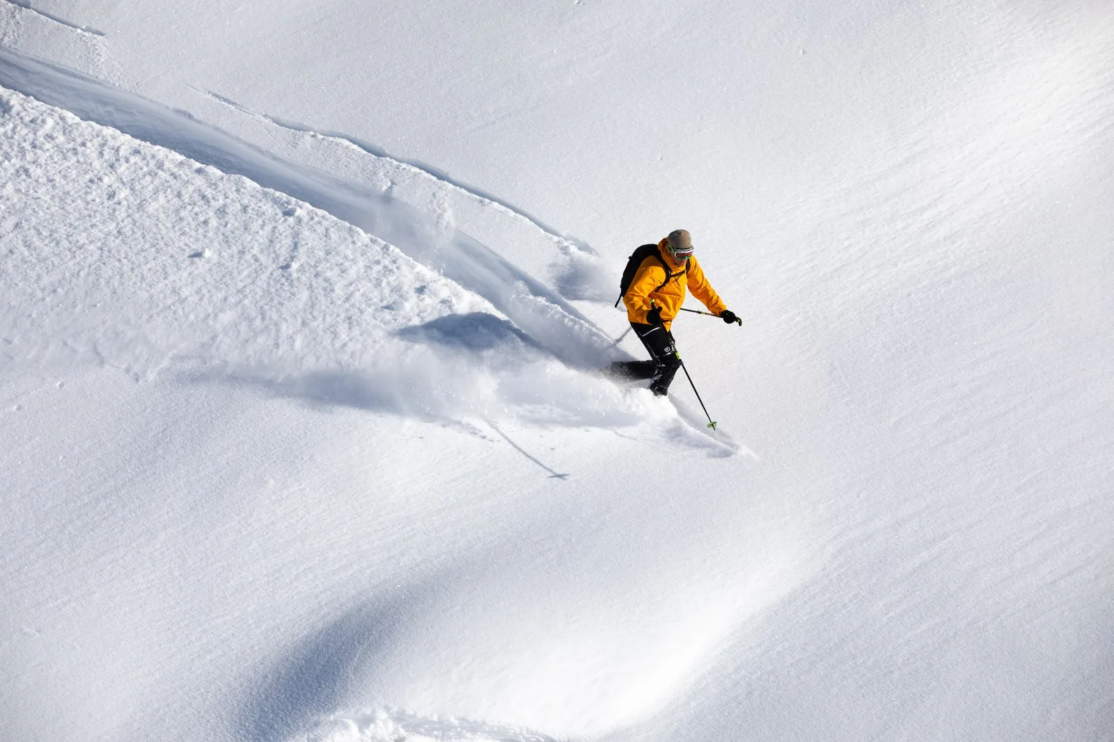 A skier descending a steep, snow-covered mountain slope in bright winter sun — winter-sports travel insurance covers the skiing injuries, mountain rescue and helicopter evacuation that standard policies leave out