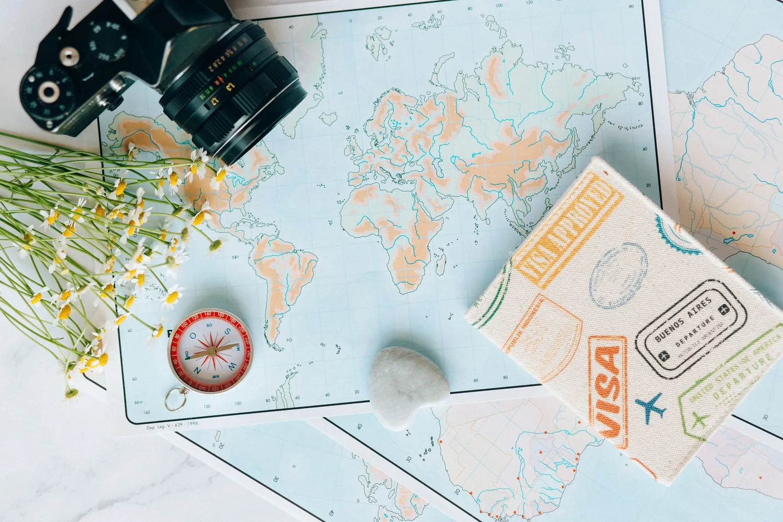 A passport resting on a world map beside travel-planning notes — checking government travel advisories before a trip