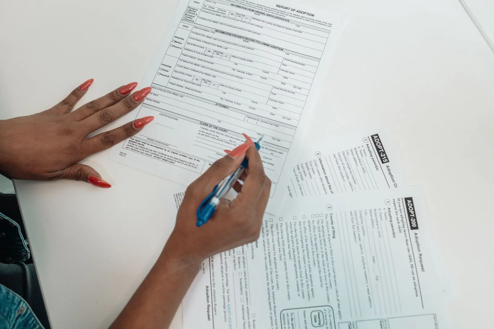 A person filling in a paper insurance claim form at a desk surrounded by receipts and supporting paperwork