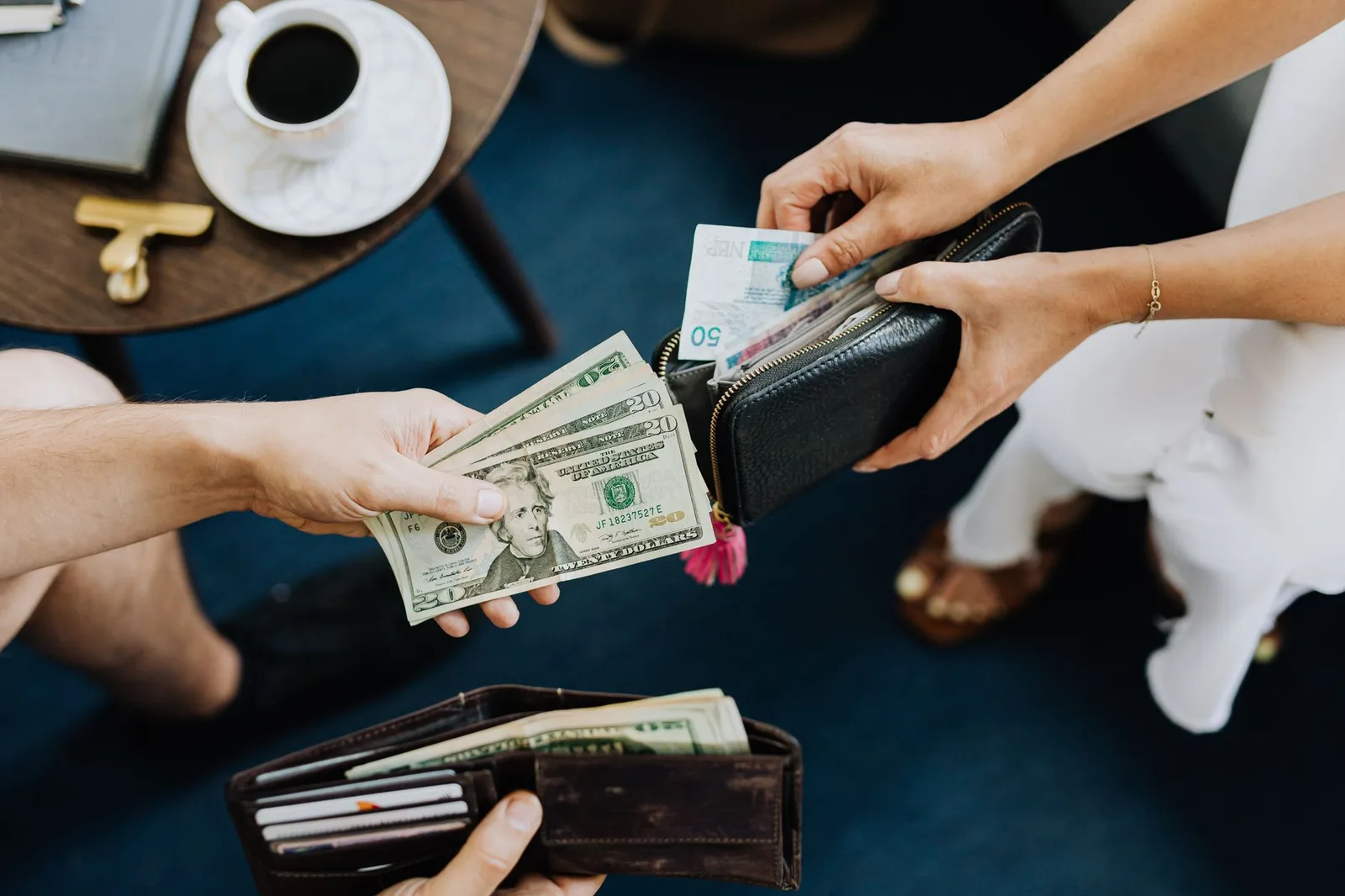 Cash banknotes of several currencies fanned out beside credit and debit cards and a wallet — the choice of how to carry and spend money abroad