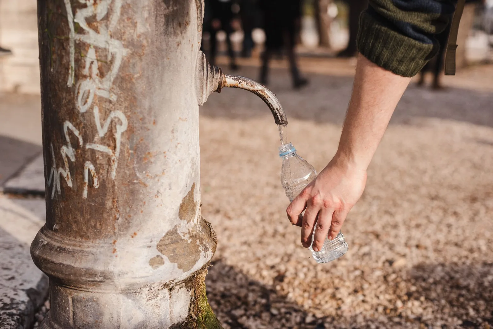 A trekker filling a reusable water bottle from a mountain stream, filtering water outdoors