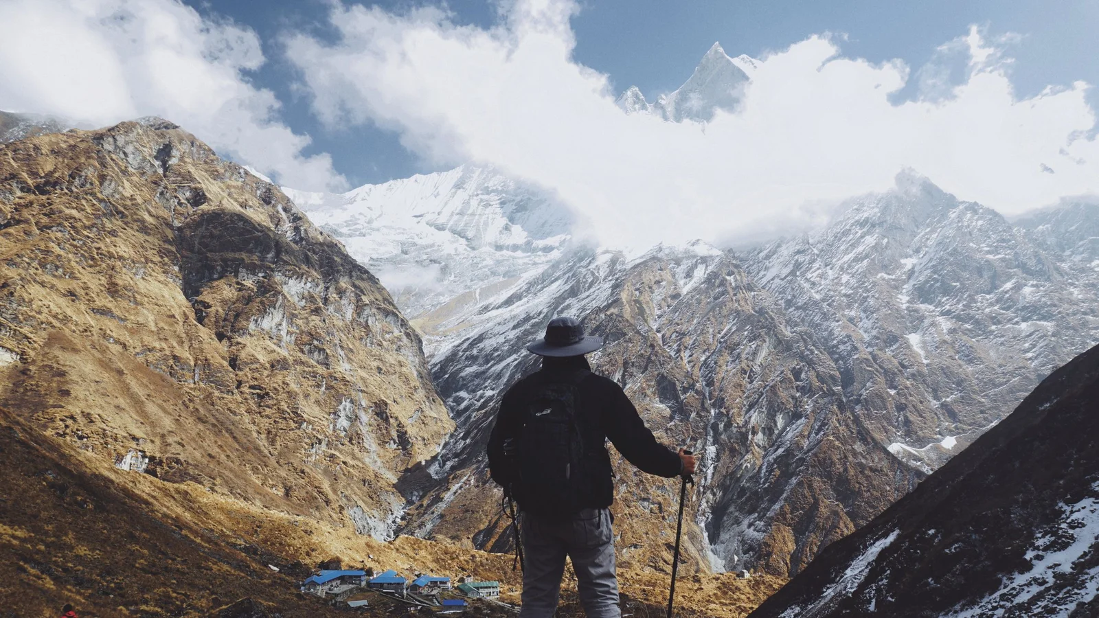 A lone hiker stands with trekking poles, admiring the breathtaking Himalayas in Nepal.
