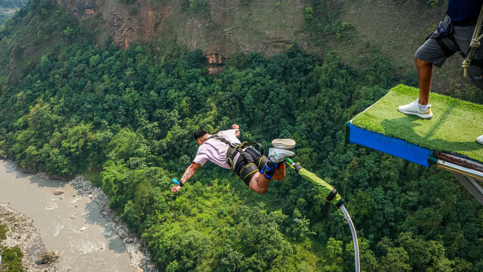 Experience the adrenaline rush of bungee jumping over a scenic canyon with dense greenery.