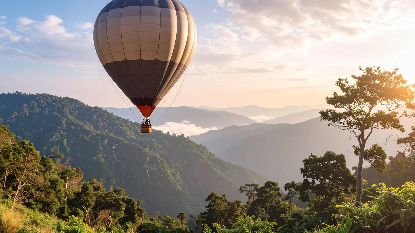 Hot air balloon drifts over lush green mountains under a clear sky at sunrise.
