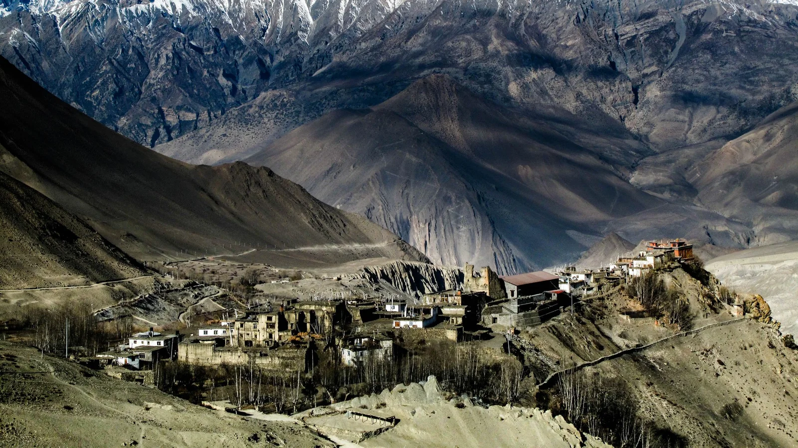 From above picturesque view of residential buildings surrounded by high rough ridge with snowy peaks under cloudless sky in winter