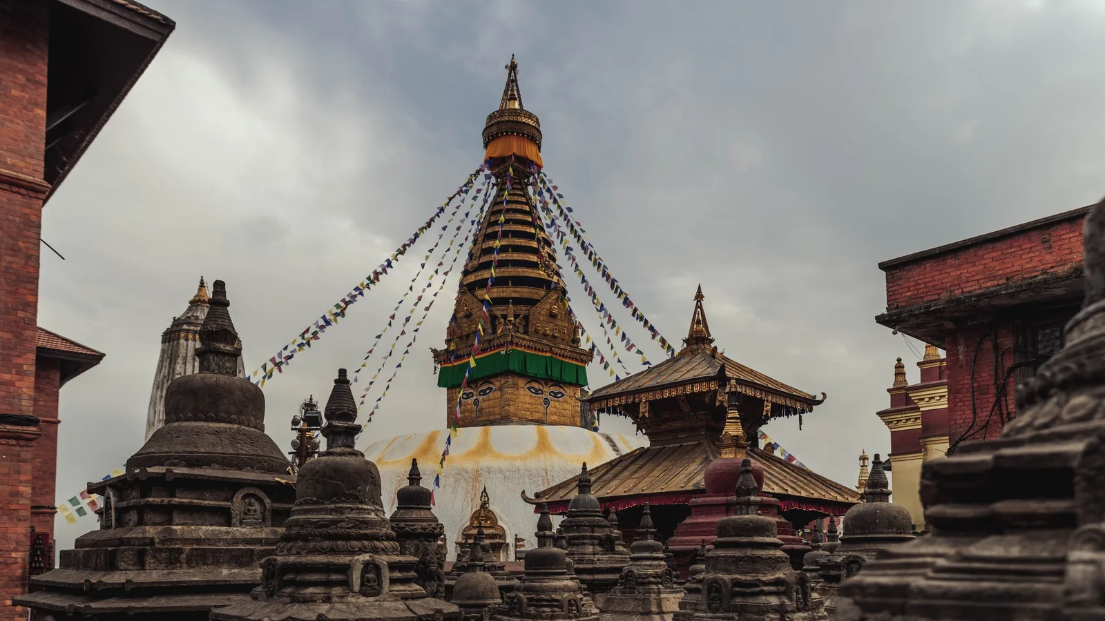 Ancient Swayambhunath Stupa in Kathmandu with vibrant prayer flags under cloudy sky.