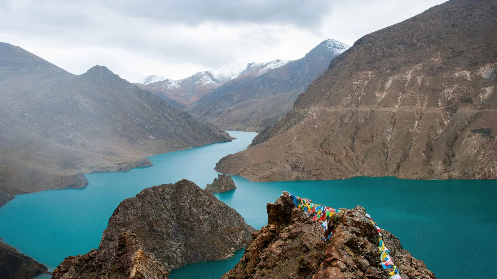 A breathtaking view of a turquoise mountain lake in the Himalayas, adorned with colorful prayer flags.