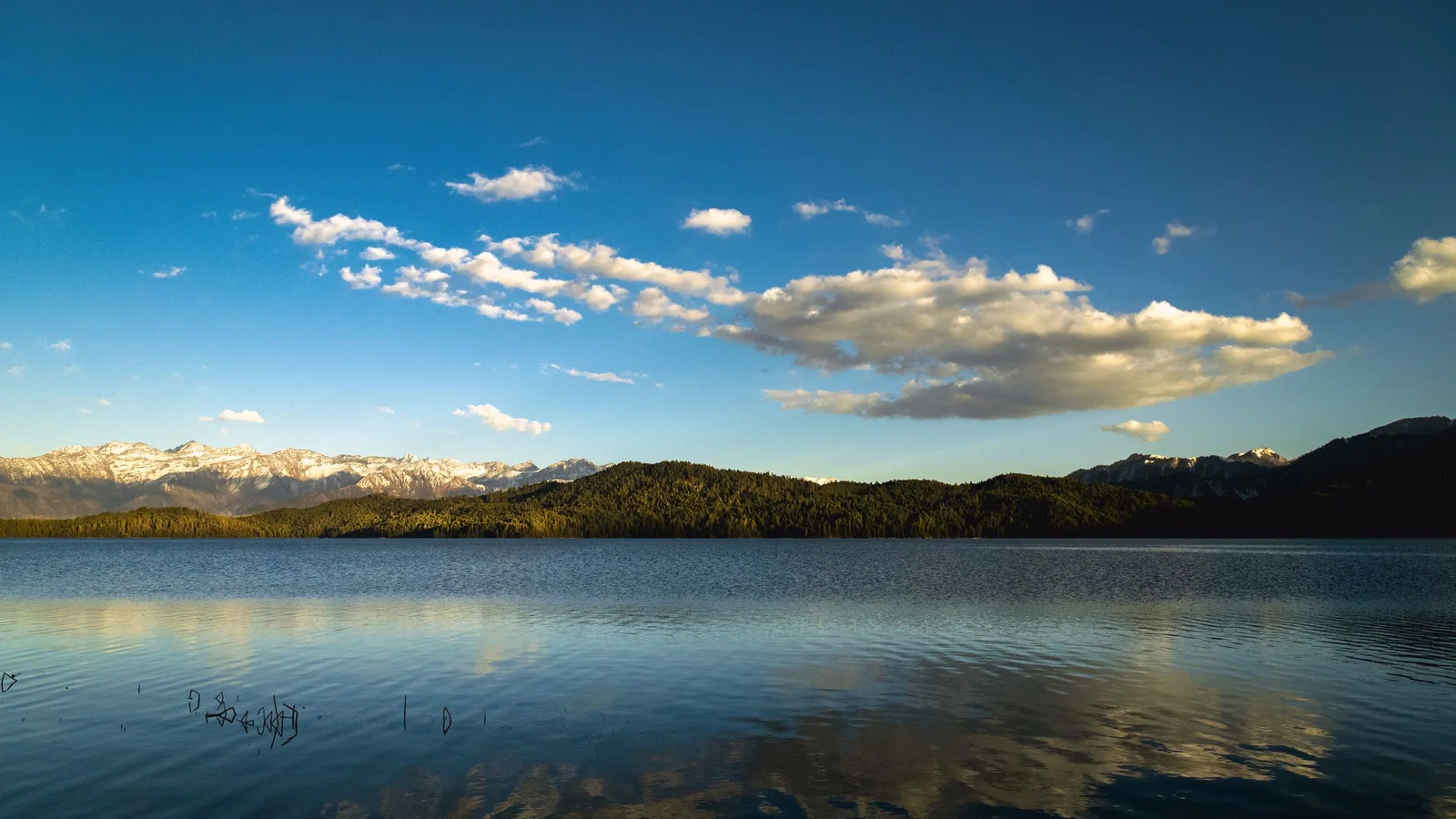 Serene view of Rara Lake with clear blue skies and reflections, surrounded by mountains in Nepal.