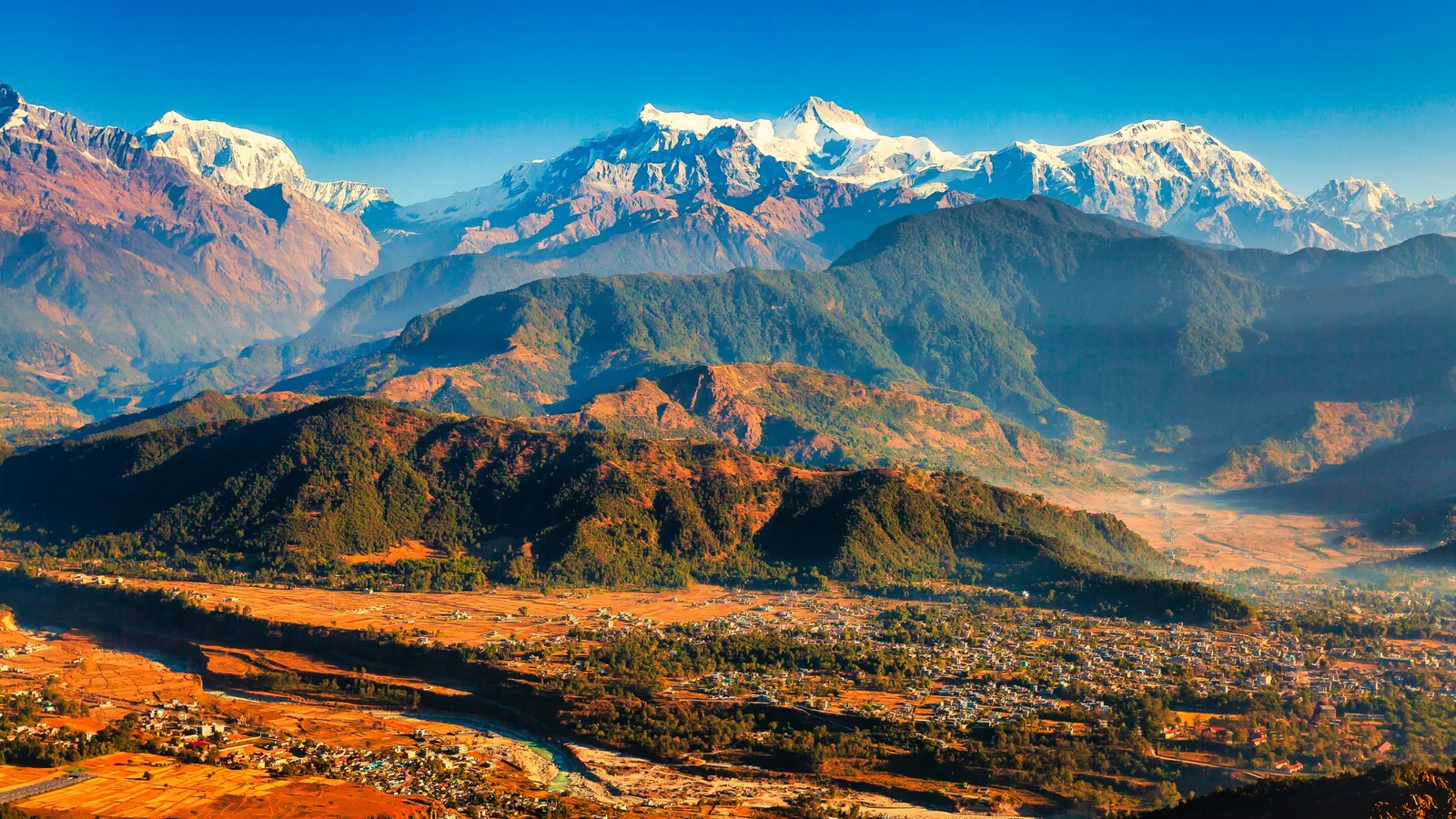 Breathtaking view of snow-capped mountains and lush valleys under a clear blue sky.