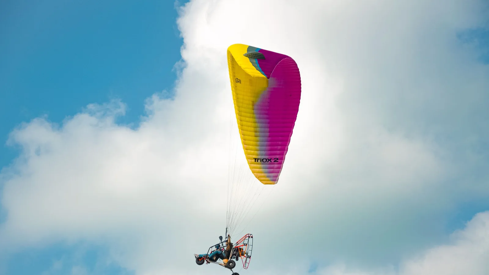 A vibrant paraglider flies against a bright blue sky, showcasing leisure and adventure.